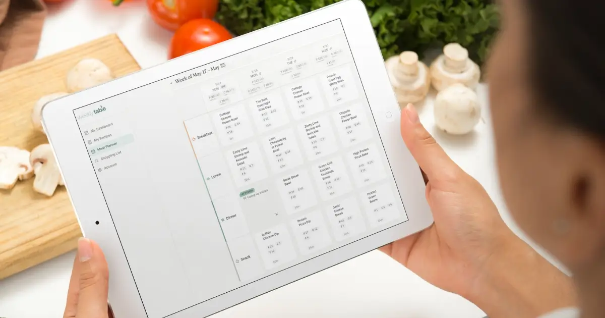 Person holding white iPad in kitchen setting looking at the Weekly Table meal planner